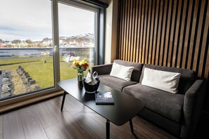 A modern living room with a grey sofa, a black coffee table, and a view of a body of water and buildings. - Rosenlund Hamn (Sande)