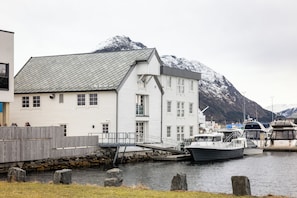 A white building with a sloped roof, a dock extending into a body of water, and boats moored nearby.