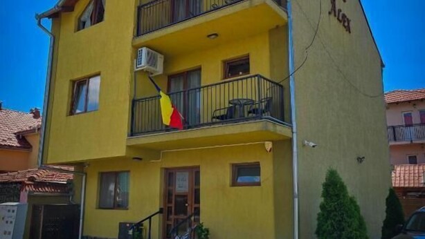 A multi-story yellow building with balconies, a motorcycle parked in front, and a small tree beside it. - Vila Alex (Tășnad)