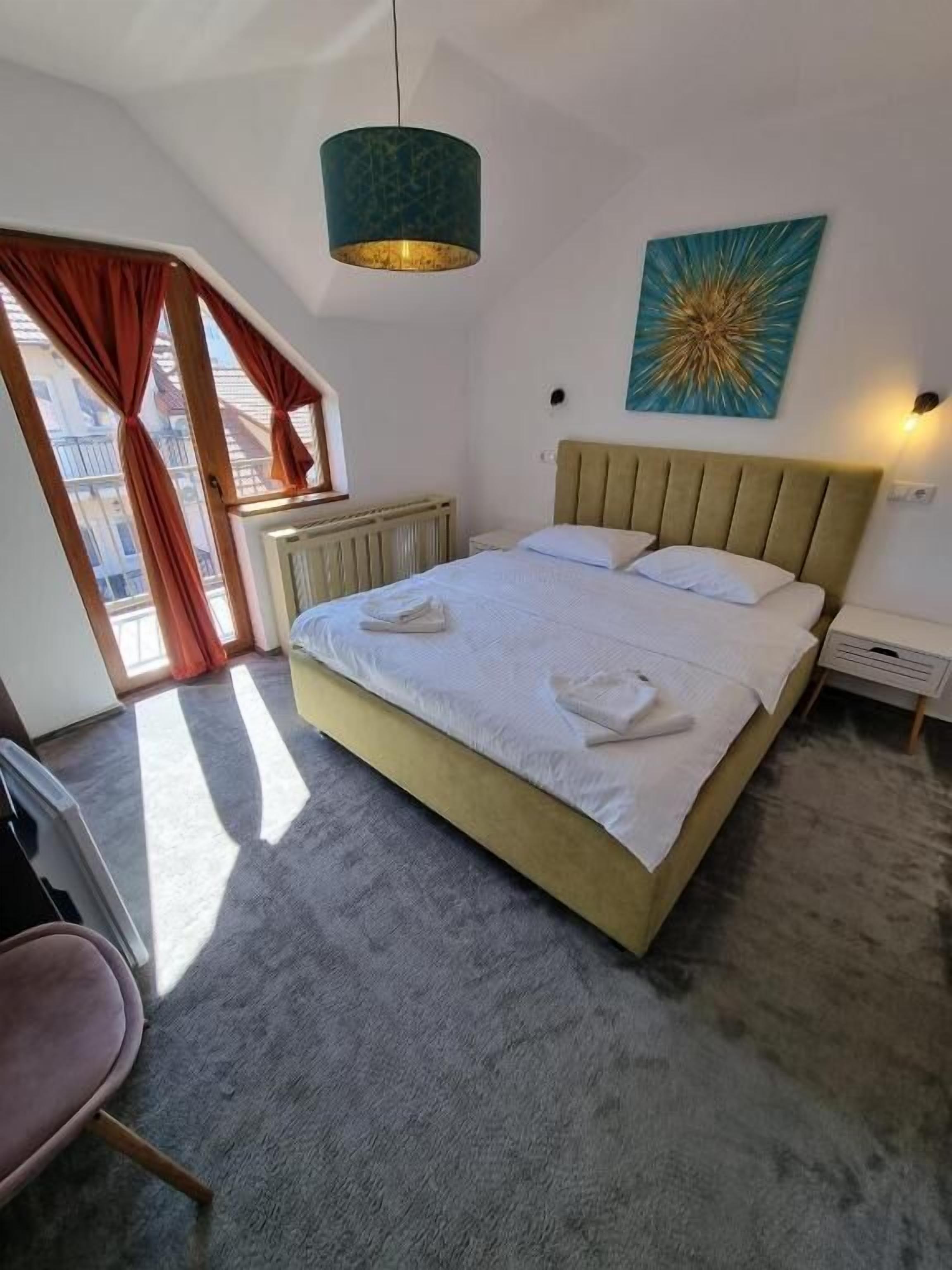 Een slaapkamer met een bed, hoofdeinde, raam met gordijnen, radiator en een wandlamp.