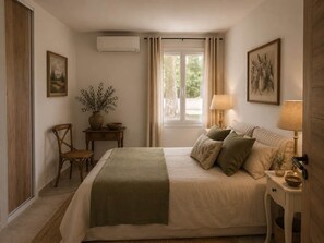 Une chambre à coucher avec un lit, une table de chevet, une lampe, une chaise et une fenêtre avec des rideaux.