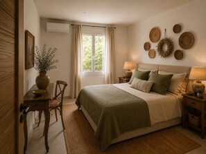 A bedroom with a bed, bedside tables, a window with curtains, a wall-mounted wreath, and a vase with a plant. - Villa du Mayoral - Domaine de Malaga - New Property (Maussane-les-Alpilles)