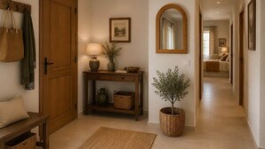Un corridoio con una porta in legno, un tavolo consolle con una lampada, uno specchio e una pianta in vaso.
