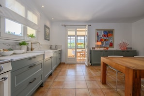 A modern kitchen with grey cabinets, a wooden dining table, and a view through an open door to a dining area. - Holiday Home 'L’Isclèze' with Mountain View, Wi-Fi and Air Conditioning (Mollans-sur-Ouvèze)