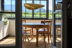 A dining area with a table and chairs, a hanging light fixture, and a view of greenery through large windows. - Holiday Home 'L’Isclèze' with Mountain View, Wi-Fi and Air Conditioning (Mollans-sur-Ouvèze)