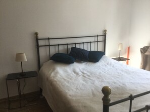 A bed with a metal frame, two pillows, a white bedsheet, a bedside table with a lamp, and a wall-mounted lamp. - Holiday Home 'L’Isclèze' with Mountain View, Wi-Fi and Air Conditioning (Mollans-sur-Ouvèze)
