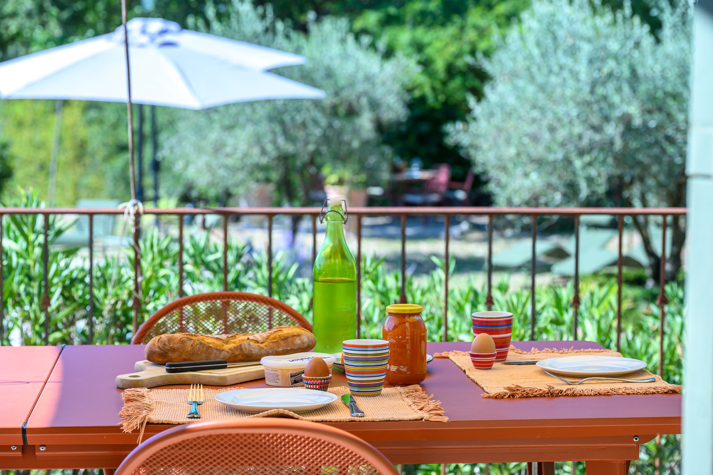 An outdoor dining setup with a table, chairs, and a view of greenery in the background.