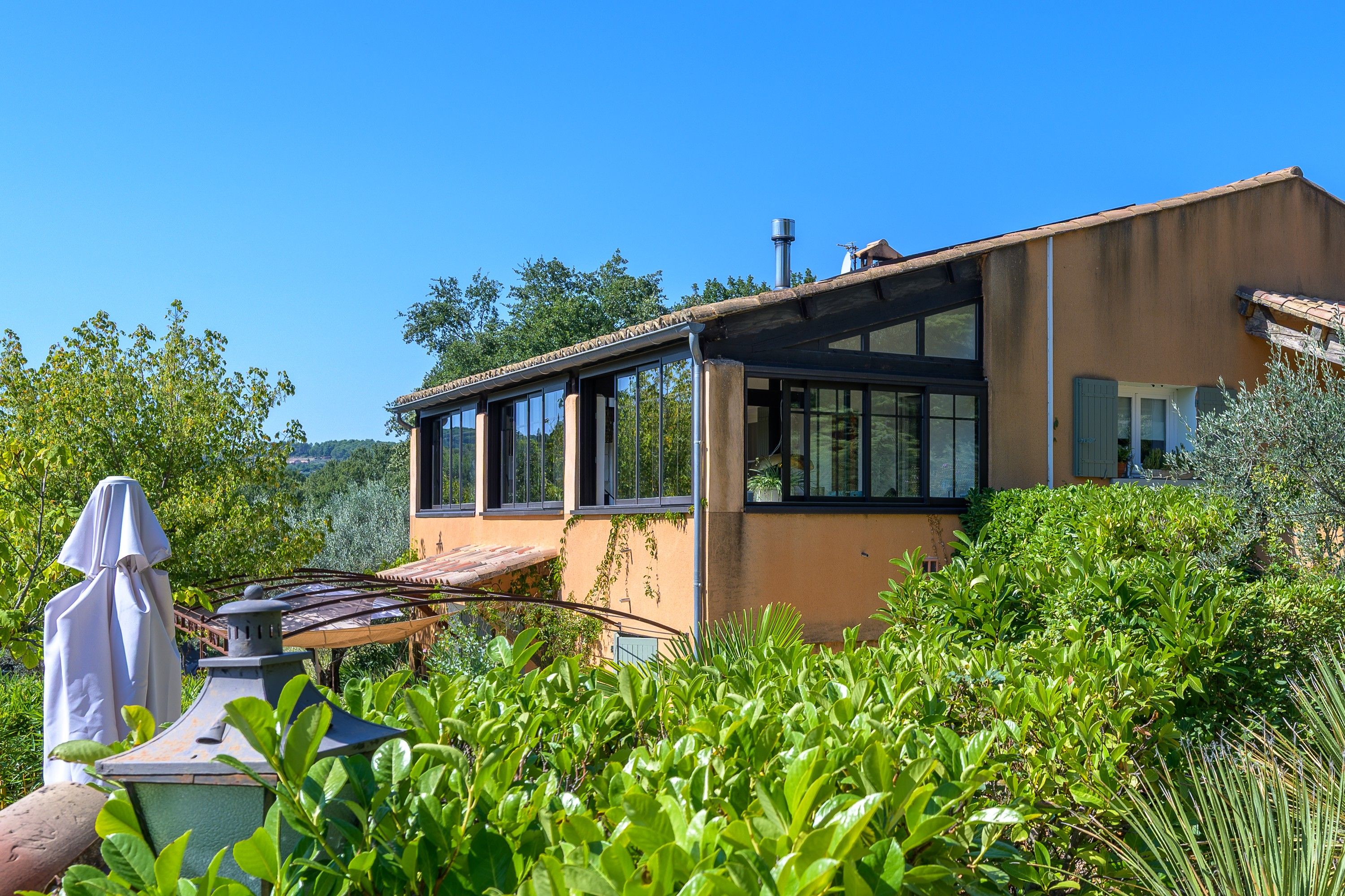 A modern house with large windows, surrounded by lush greenery.