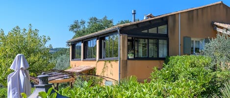 A modern house with large windows, surrounded by lush greenery.