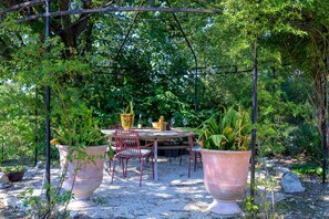 An outdoor dining area with a table and chairs, surrounded by large planters and trees. - Holiday Home 'L’Isclèze' with Mountain View, Wi-Fi and Air Conditioning (Mollans-sur-Ouvèze)