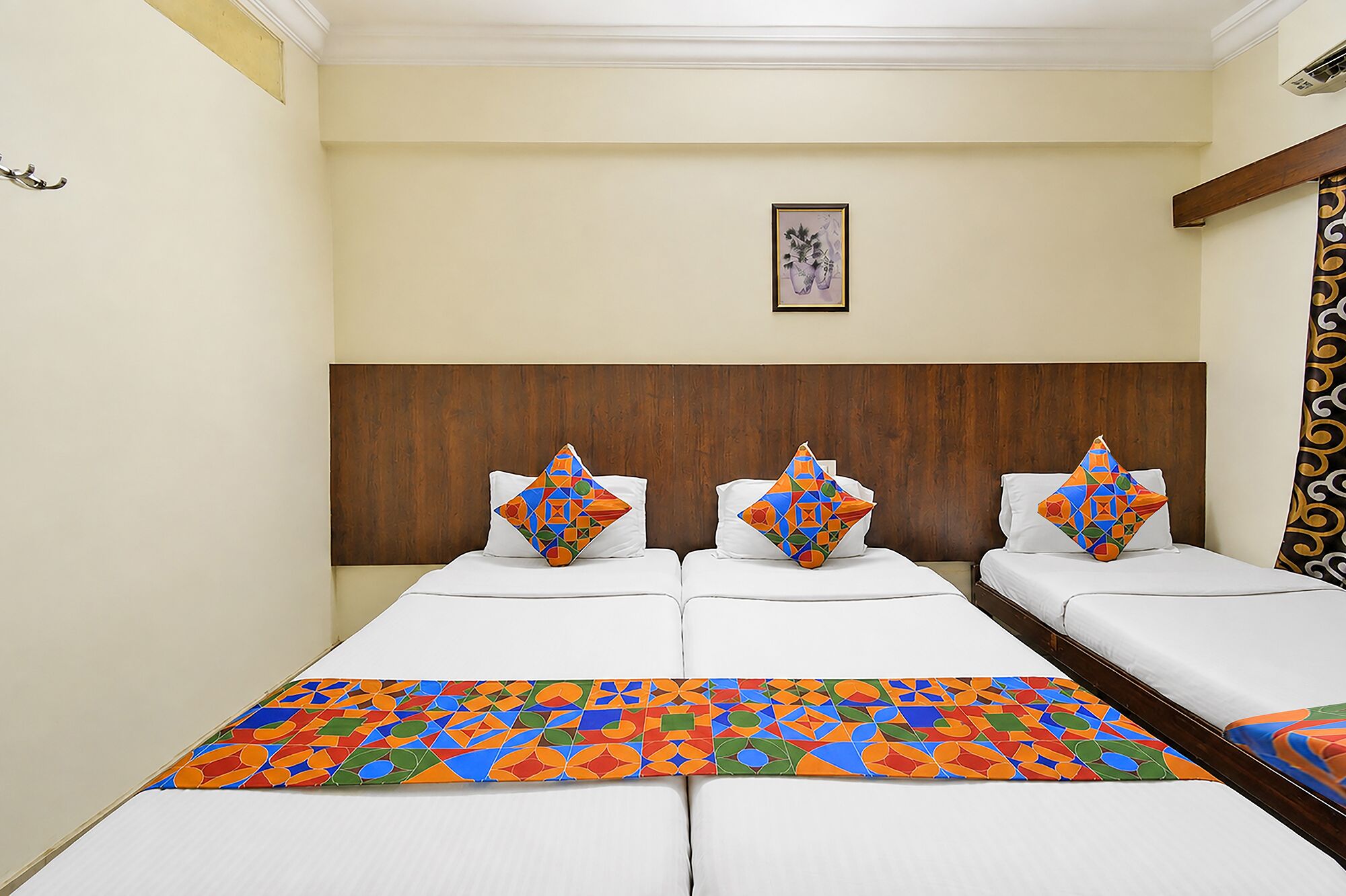 Quarto de hotel com cabeceira de madeira, cama com almofadas estampadas em padrões geométricos coloridos e um quadro na parede.