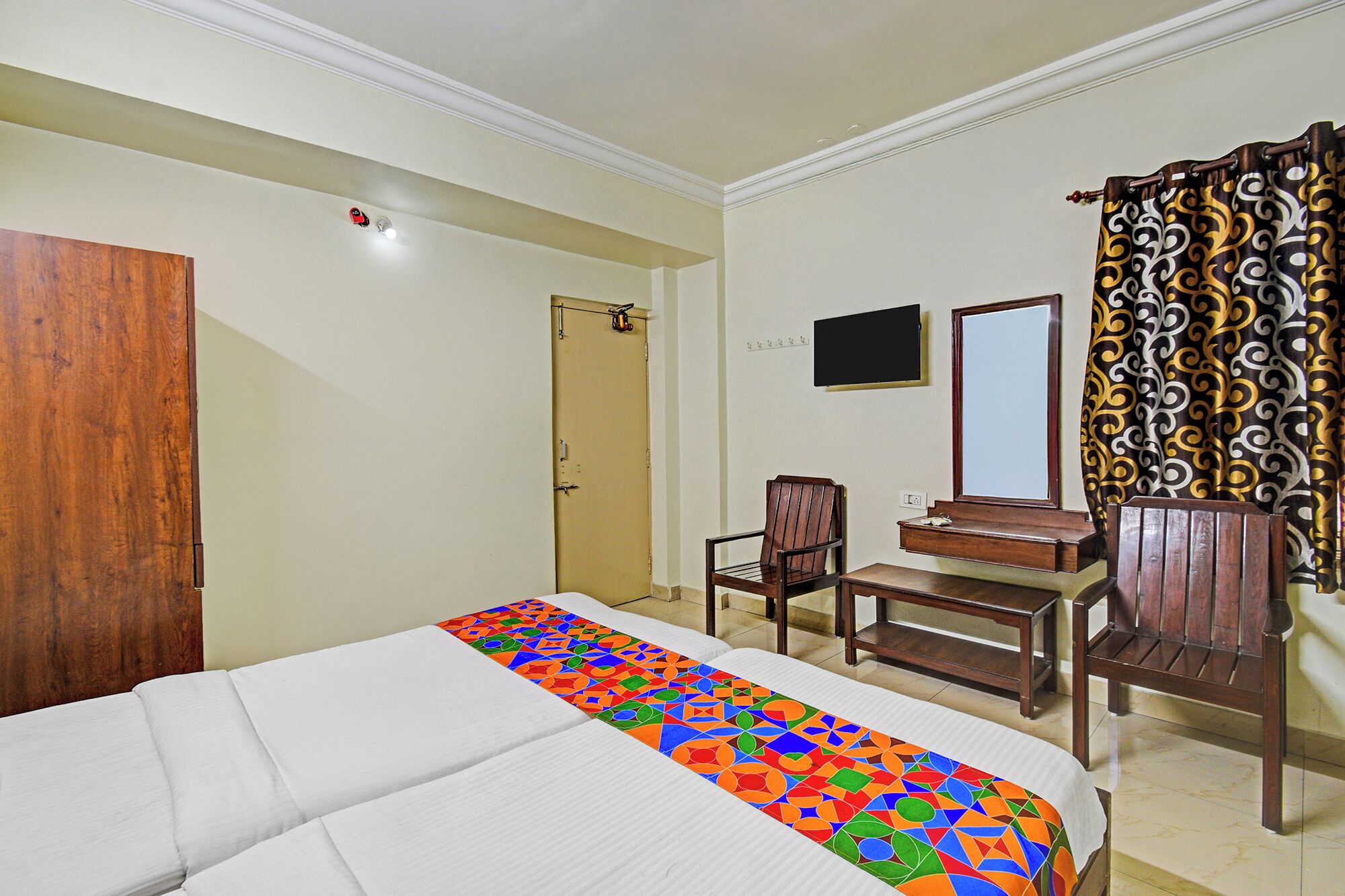 A hotel room with a bed, a desk, a chair, a wardrobe, a mirror, and a television.