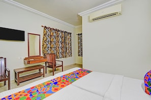 Una habitación de hotel con cama, escritorio, silla, espejo y cortinas estampadas.