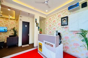 Et hotellets receptionområde med en reception, skiltet 'fab hotels', et vægmonteret fjernsyn og et mønstret tapet.