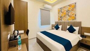 Habitación de hotel con cama, mesita de noche, escritorio con silla, botella de agua, unidad de aire acondicionado y un cuadro en la pared.