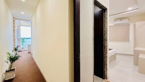 Un pasillo con una planta en maceta, una puerta y una vista parcial de un baño con bañera.