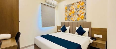 A hotel room with a bed, bedside table, chair, and an air conditioning unit.