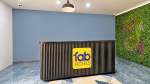 Un comptoir d’accueil avec une enseigne indiquant « fab hotels », un luminaire au plafond et un mur vert orné d’un motif de feuilles.