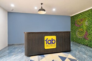 Una recepción con un cartel de 'fab hotels', una lámpara en el techo y una pared verde con un diseño de hojas.