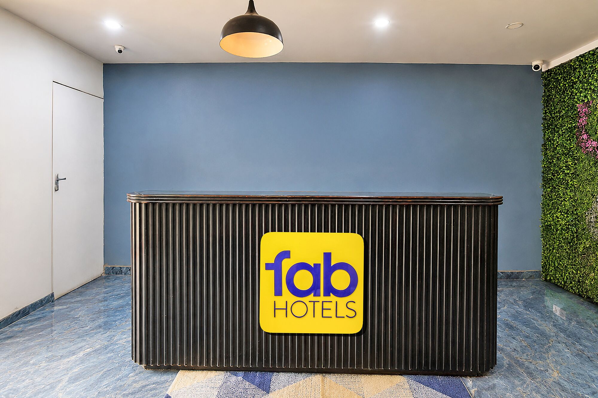 A reception desk with a sign for 'fab hotels' in a room with a blue wall and a green plant wall.