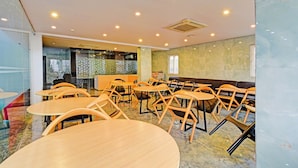 Un grand espace intérieur aménagé avec différents types de sièges, notamment des tables et des chaises rondes, et une cuisine ouverte visible au fond.