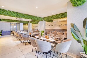 A modern dining area with a long table, cushioned chairs, and a green wall. - Fabhotel Imperial Executive (Mumbai)