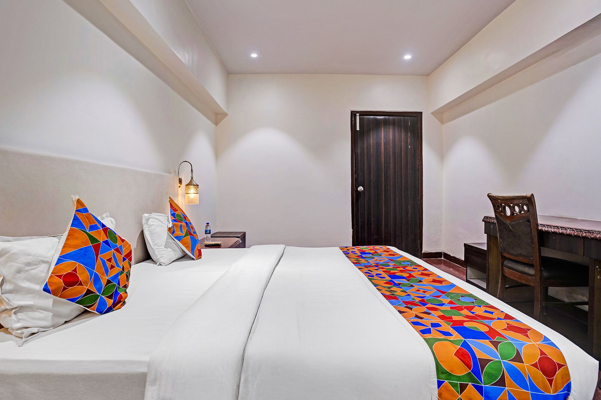A hotel room with a bed, a desk, a chair, and a door.