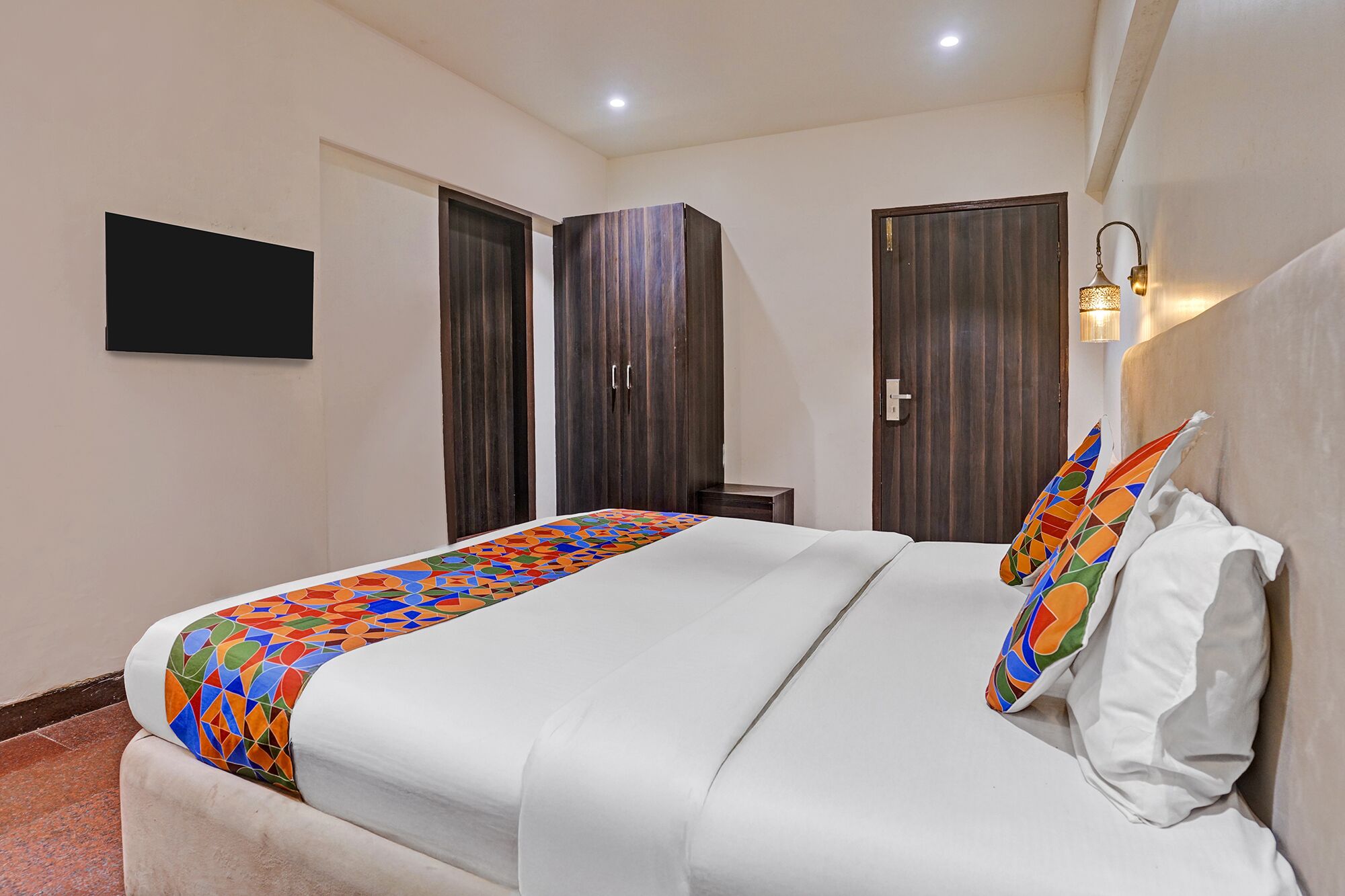 A hotel room with a bed, a TV mounted on the wall, and a bedside lamp.