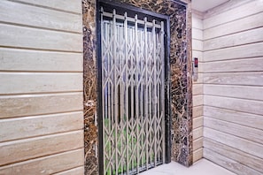 A door with a metal gate, a marble-like textured wall, and a corner with a light-colored floor. - Fabhotel Imperial Executive (Mumbai)