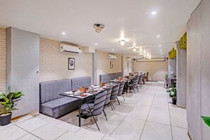 A restaurant with a long counter, grey upholstered seating, and multiple tables. - FabHotel Imperial Executive (Mumbai)