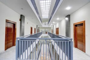 A modern hotel corridor with a central staircase, wooden doors, and a skylight. - FabHotel Royal Inn (Noida)