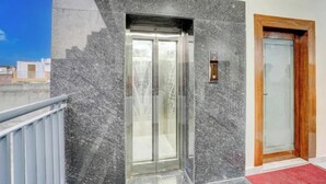 Een moderne lift met glazen deur, houten deur en een marmeren wand.