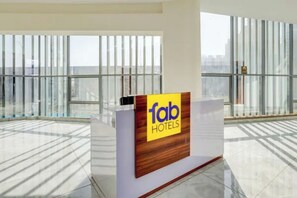 A reception desk with a sign for Fab Hotels, large windows, and a tiled floor. - FabHotel Royal Inn (Noida)