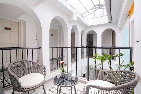 A balcony with wicker chairs, a glass table, and potted plants.