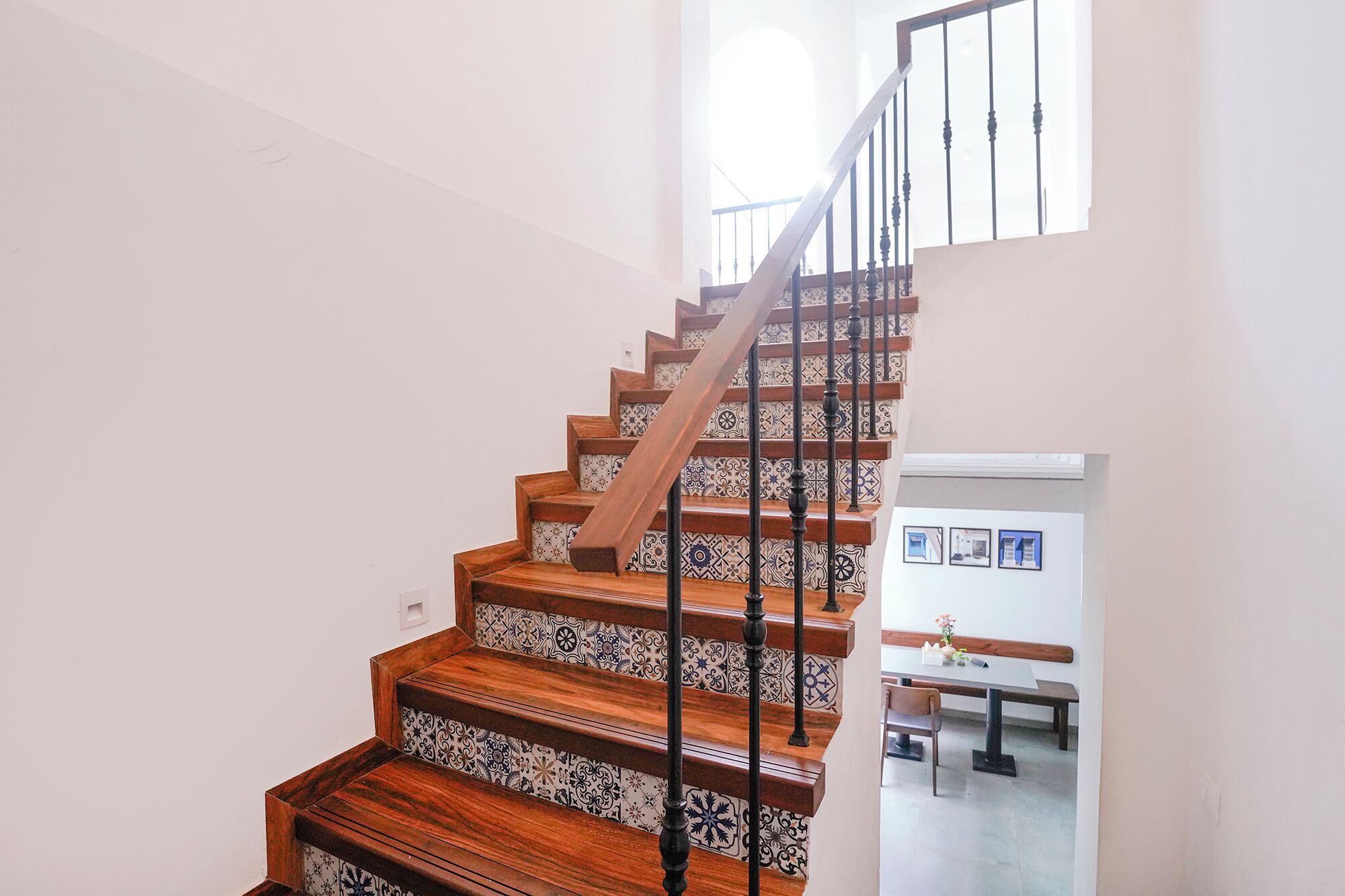 Una escalera de madera con barandilla negra, que conduce a un rellano con pared blanca y una ventana.