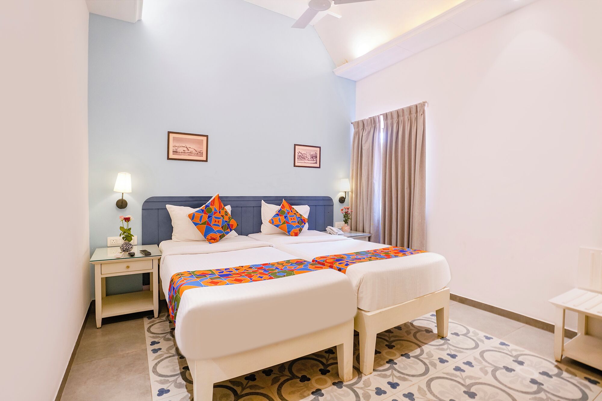 A hotel room with a bed, bedside tables, a nightstand, a lamp, and a window with curtains.
