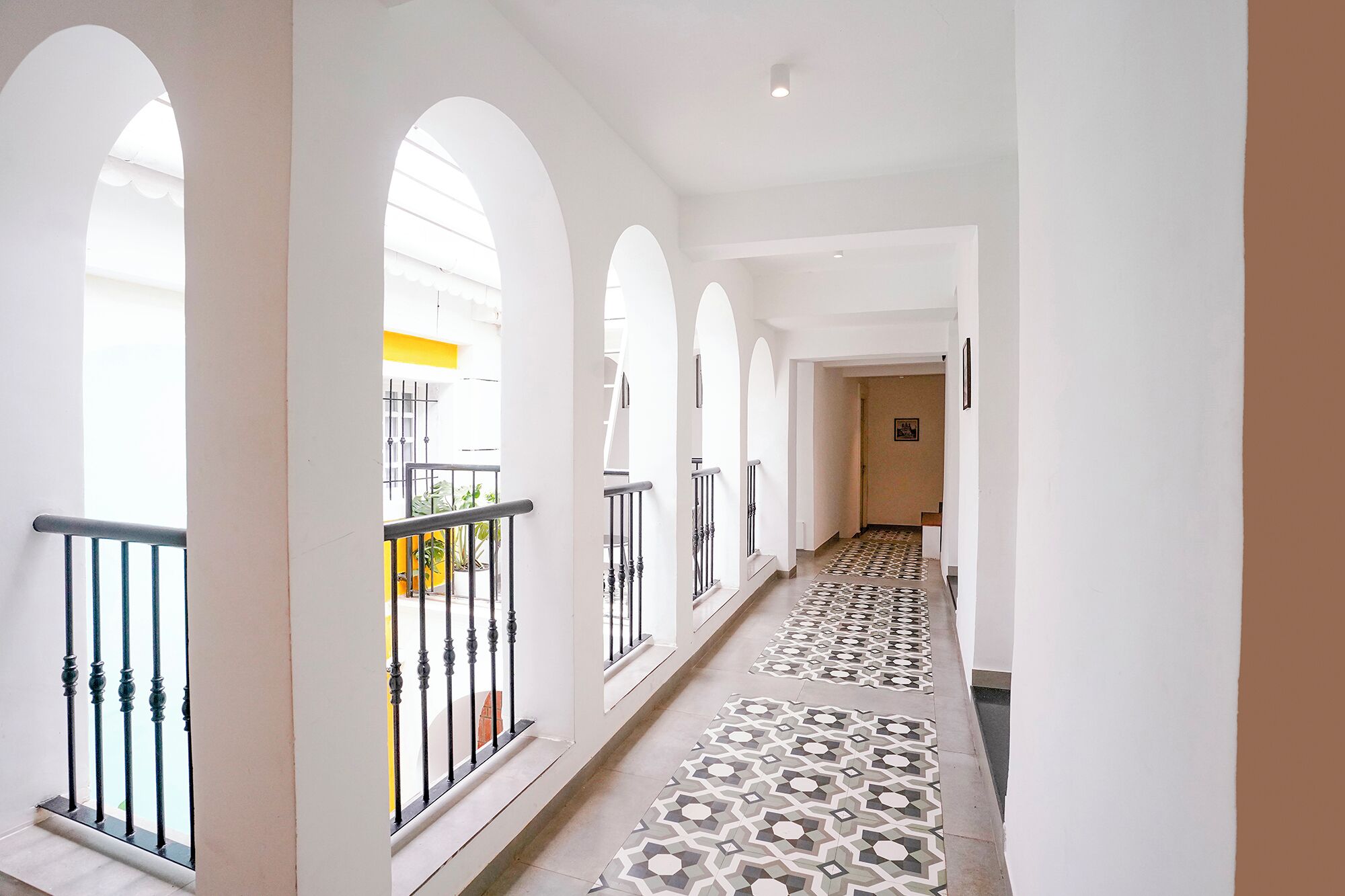 A corridor with white walls, black railings, and patterned floor tiles.
