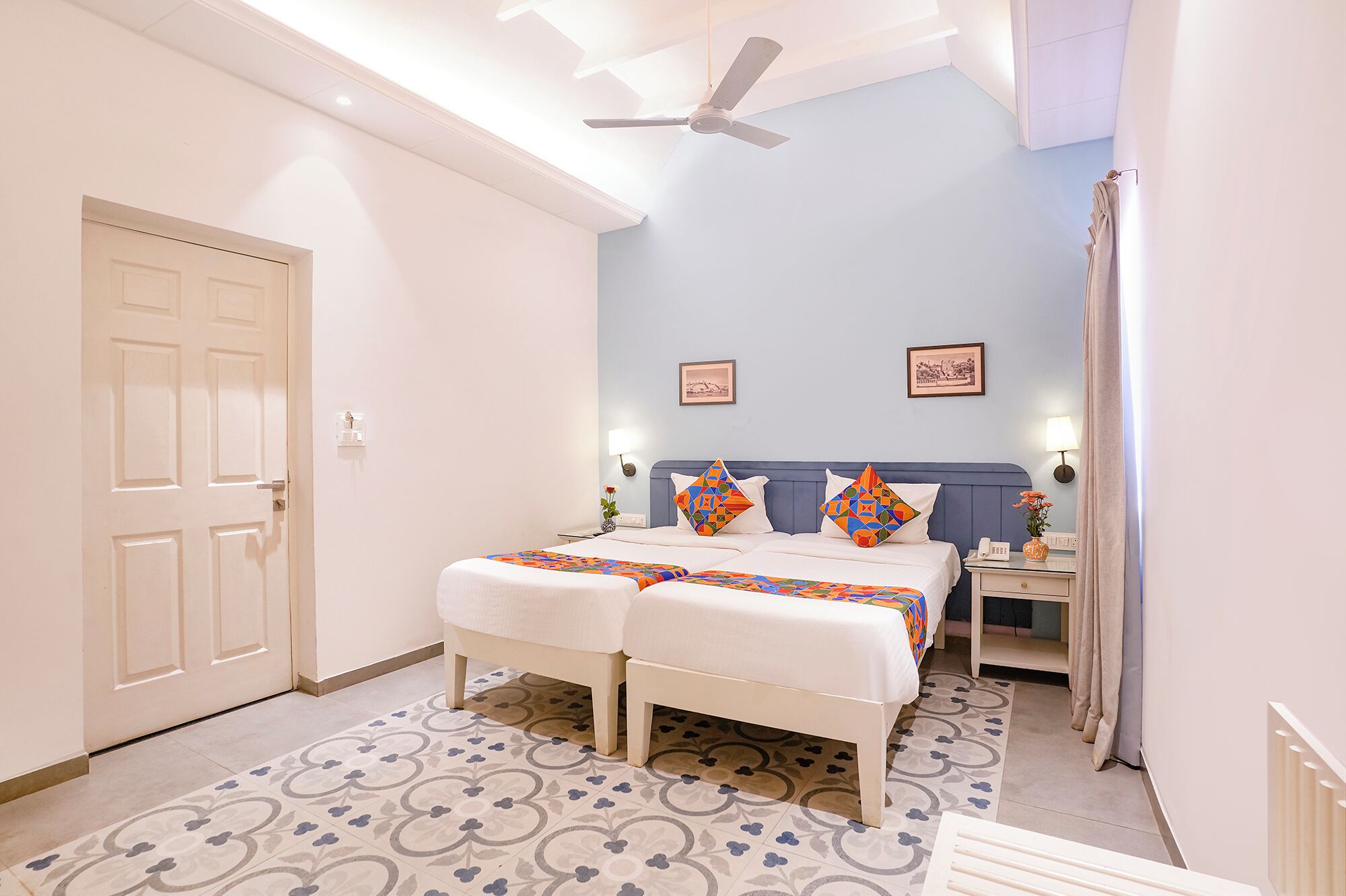 A hotel room with a bed, bedside tables, a ceiling fan, and patterned floor tiles.