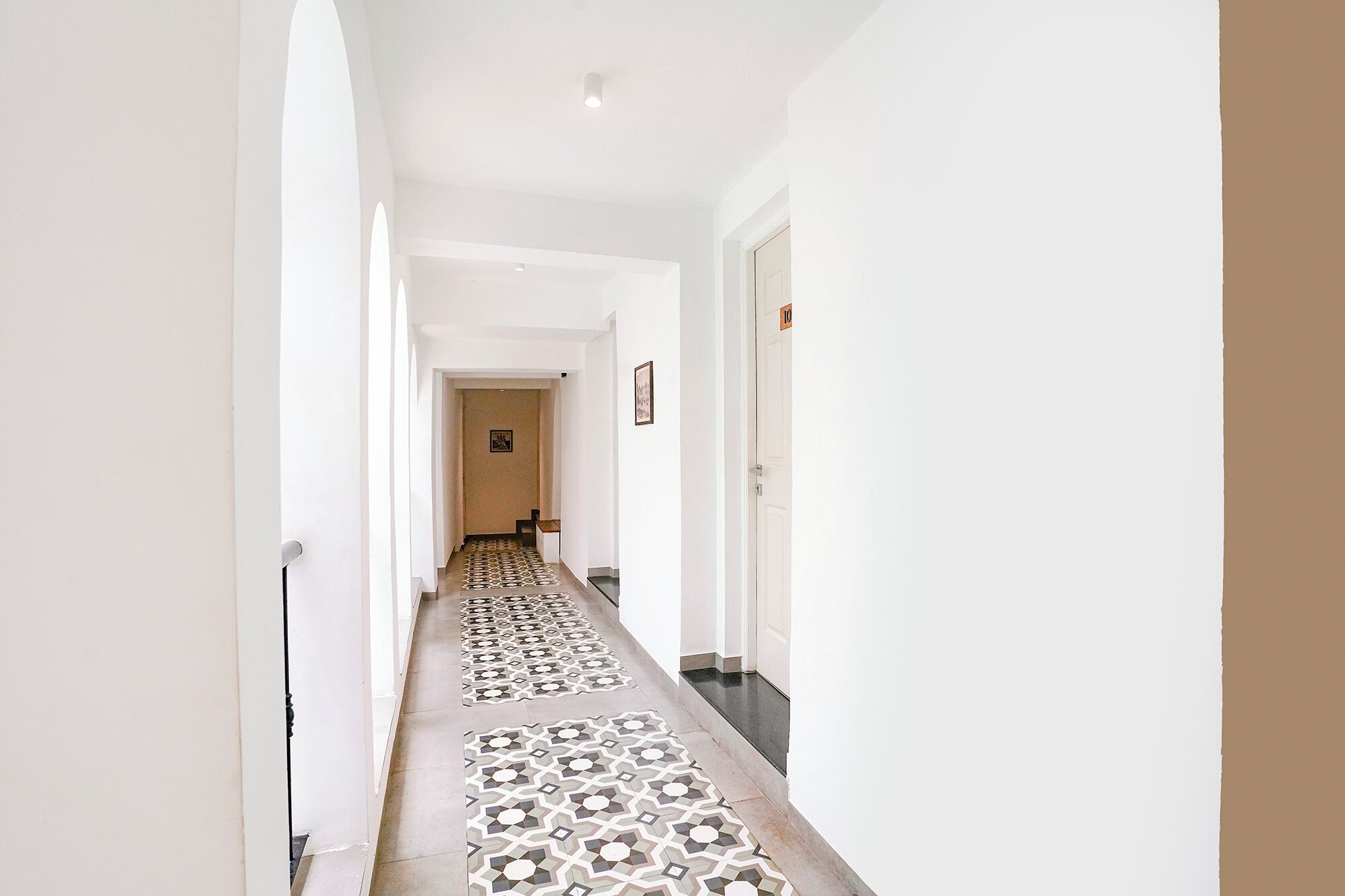 A hallway with patterned flooring, white walls, and a door with a number sign.