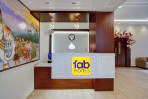 A reception desk with a logo for 'fab hotels', a clock, and a decorative wall painting. - FabHotel SV Grand I - 1 KM From Kashi Vishwanath Temple (Varanasi)
