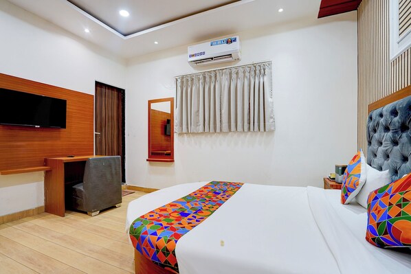 A hotel room with a bed, a TV mounted on the wall, an air conditioning unit, a mirror, and a window with curtains. - FabHotel SV Grand I - 1 KM From Kashi Vishwanath Temple (Varanasi)