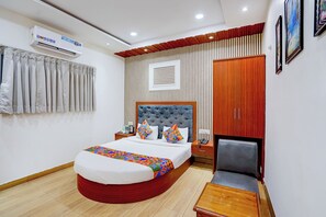A hotel room with a bed, bedside table, chair, wardrobe, and an air conditioning unit. - FabHotel SV Grand I - 1 KM From Kashi Vishwanath Temple (Varanasi)