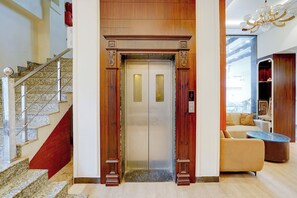 An elevator with a digital display, a staircase with marble steps, and a modern interior with a sofa and a glass coffee table. - FabHotel SV Grand I - 1 KM From Kashi Vishwanath Temple (Varanasi)