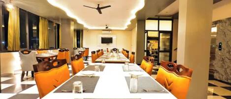 A hotel dining room with a long table, orange chairs, and a ceiling fan.