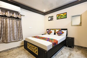Quarto de hotel com cama, mesa de cabeceira, relógio de parede, quadro e espelho.