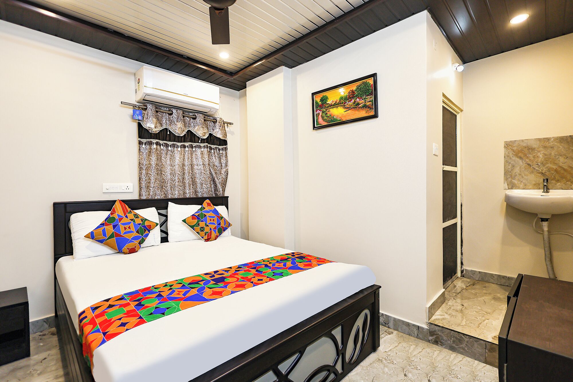 Habitación de hotel con una cama, un cuadro, un baño con lavamanos y un equipo de aire acondicionado.