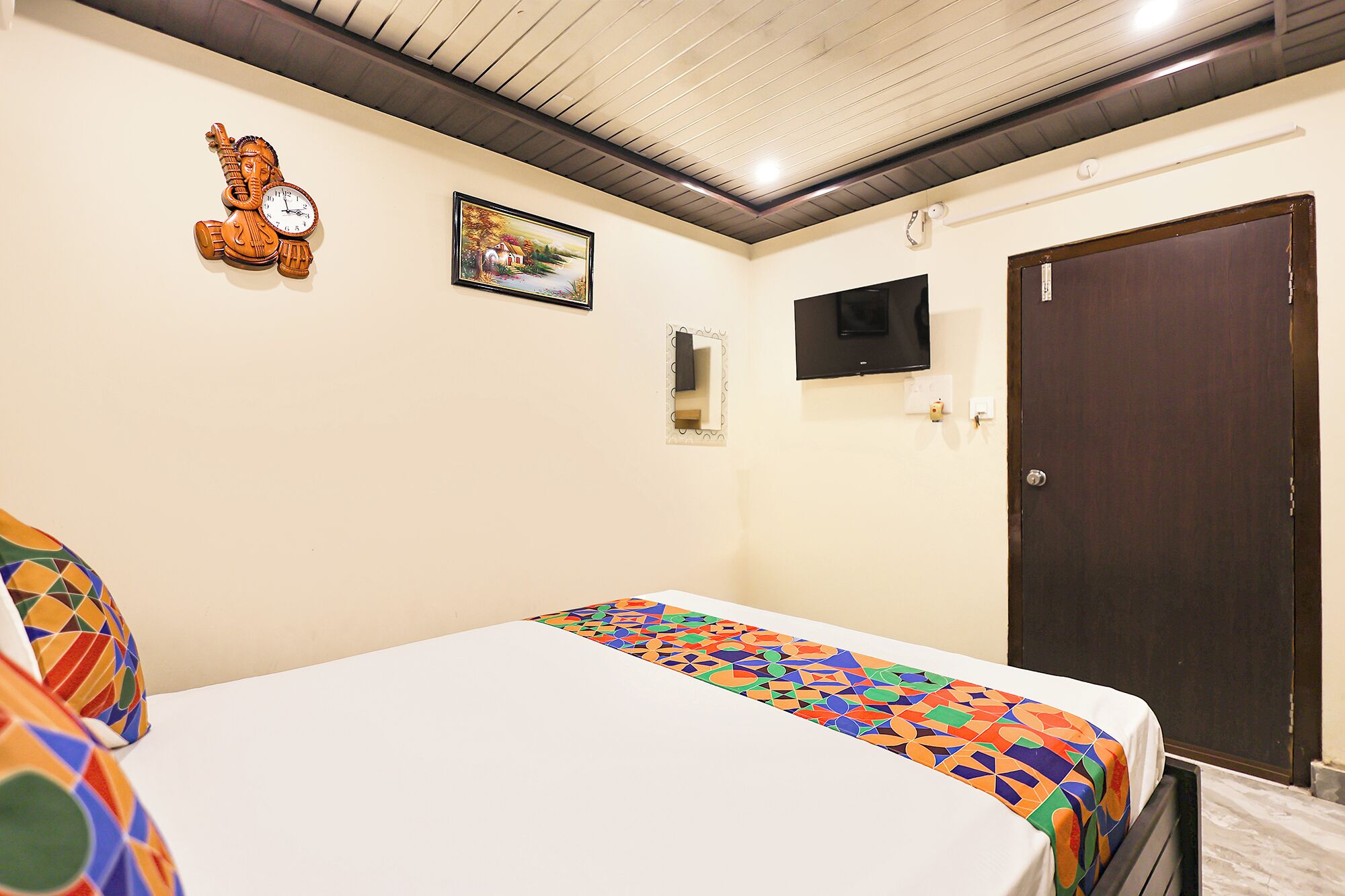 A hotel room with a bed, a TV, a door, and a wall clock.