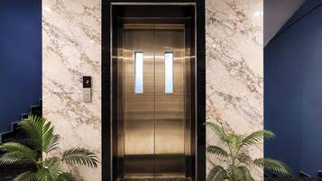 An elevator with a metallic finish, flanked by marble walls and blue accents.