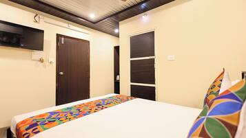 A hotel room with a bed, a television mounted on the wall, a door, and a shelf unit.