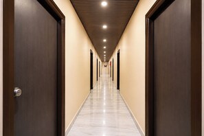 Corredor de hotel com portas em ambos os lados, piso ladrilhado e iluminação embutida no teto.